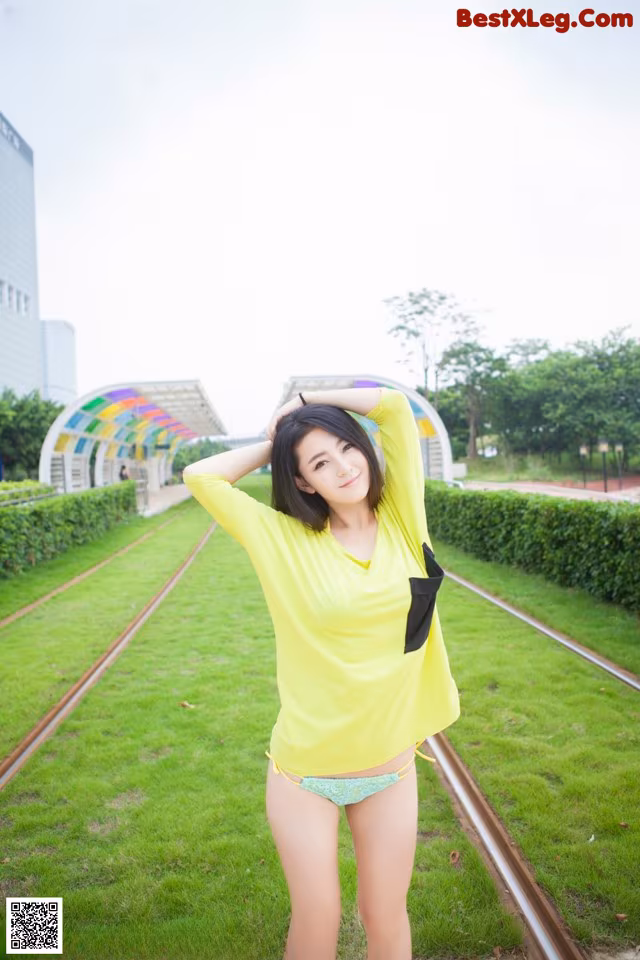 A woman in a yellow shirt and blue panties posing on a train track.