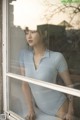 A woman in a blue bodysuit leaning against a window.