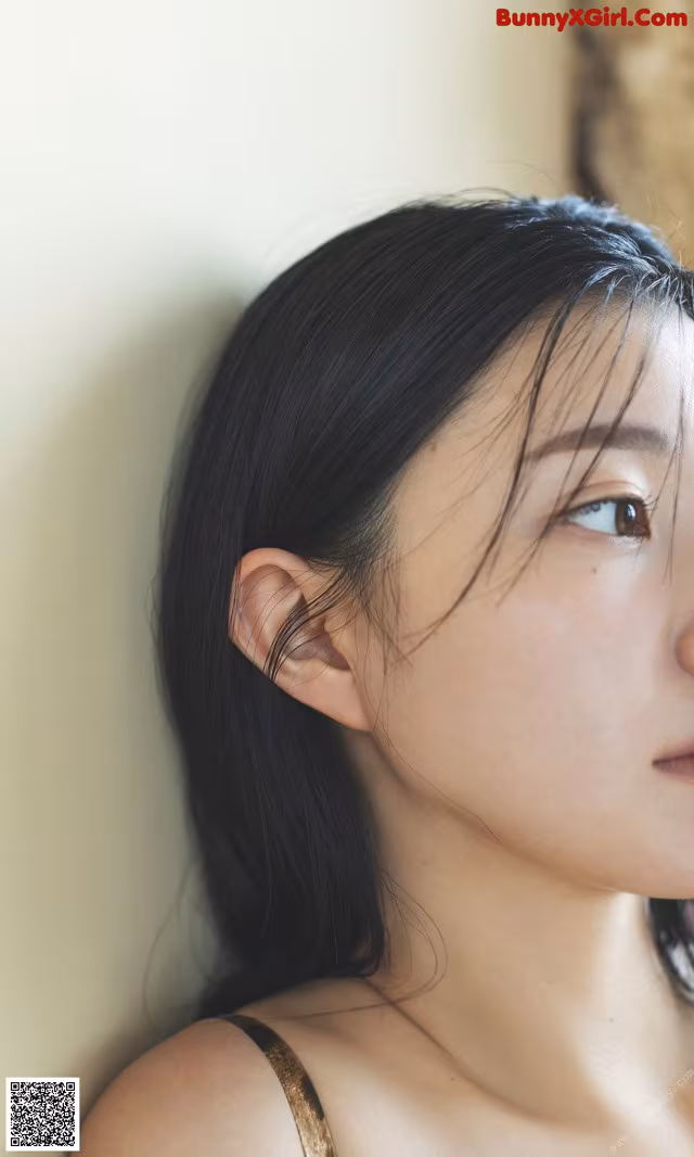 A woman with long black hair leaning against a wall.