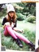 A woman sitting in the grass wearing pink tights and a baseball cap.