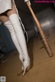 A woman in white thigh high boots holding a baseball bat.