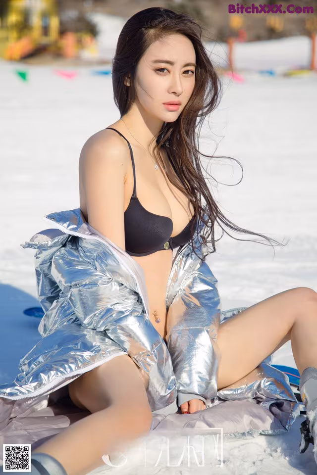 A woman in a black bikini sitting in the snow.