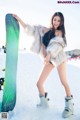 A woman standing in the snow holding a snowboard.