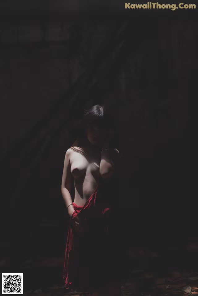 A naked woman in a red dress standing in a dark room.