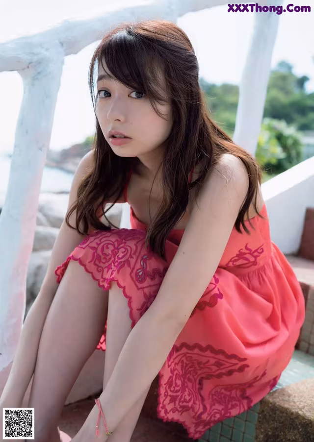 A woman in a pink dress sitting on a ledge.