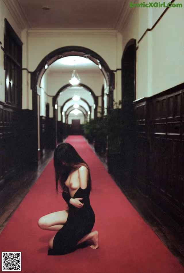A woman in a black dress crouching down on a red carpet.