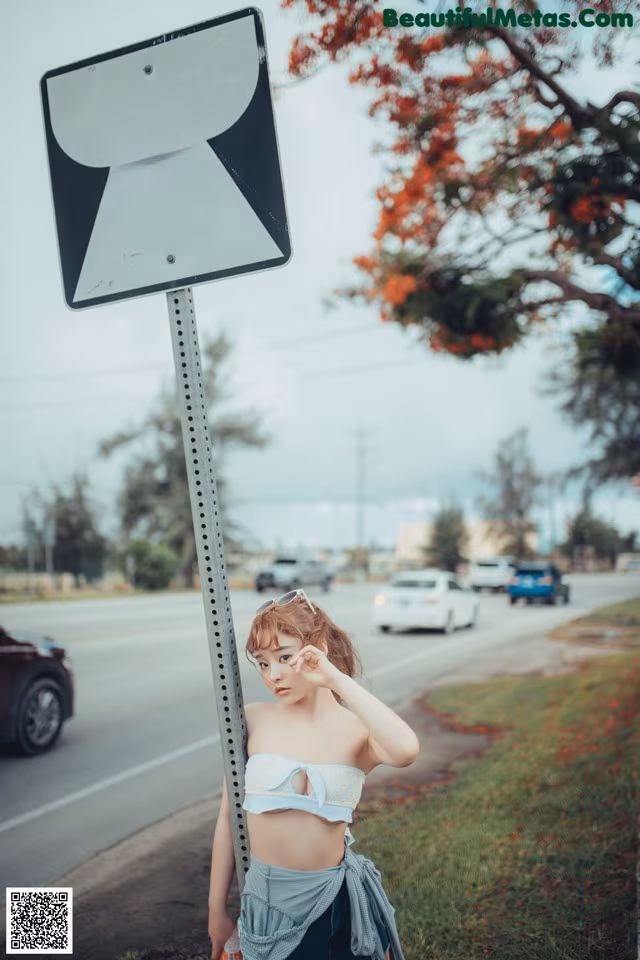 A woman standing next to a road sign on the side of the road.