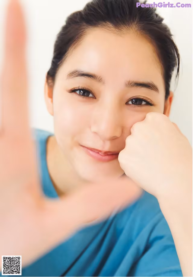 A woman in a blue shirt is making a peace sign.