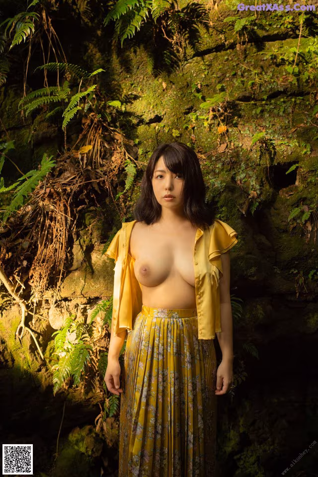 A woman in a yellow shirt and skirt standing in a forest.
