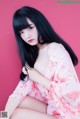 A woman in a pink kimono sitting on a pink background.