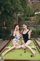 Two women sitting on a pool table with balls.