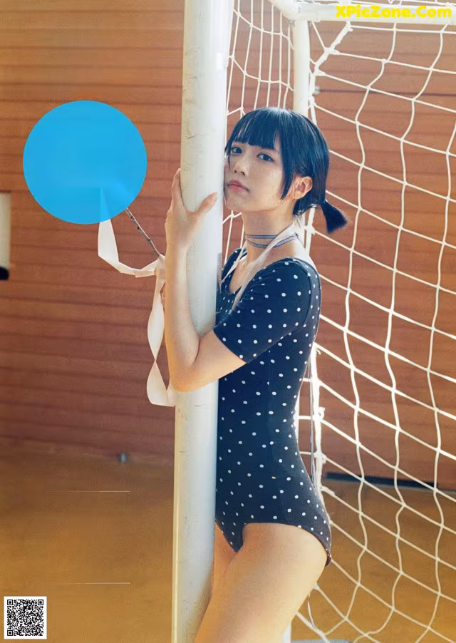 A woman in a polka dot bathing suit leaning against a pole.