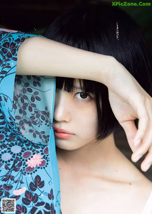 A woman in a blue and black floral dress is posing for a magazine.