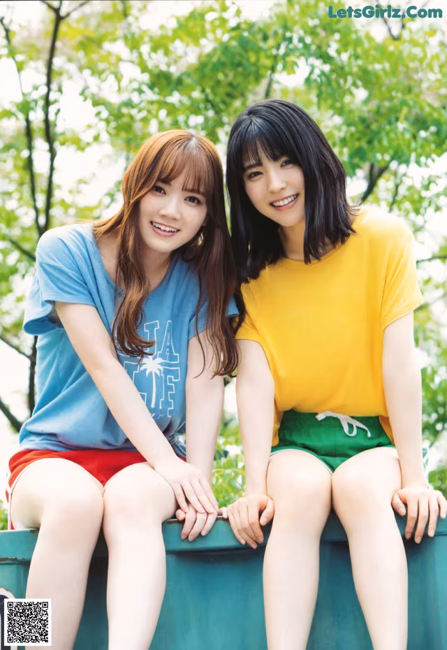 Two young women sitting on top of a green trash can.