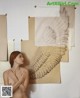 A nude woman standing in front of a drawing of an angel wing.