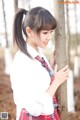 A young woman in a school uniform leaning against a tree.