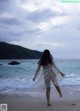 A woman walking on the beach in a sheer white dress.