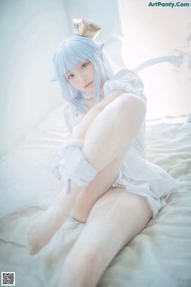 A woman in a white dress sitting on a bed.