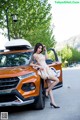 A woman in a dress leaning on the hood of a car.