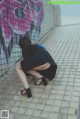 A woman crouching down in front of a graffiti covered wall.