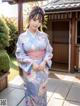 A woman in a blue kimono standing in front of a house.